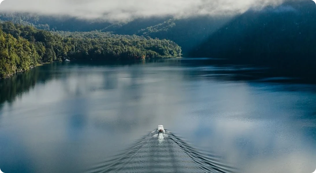 Embarcación navegando un lago patagónico entre bosques y montañas